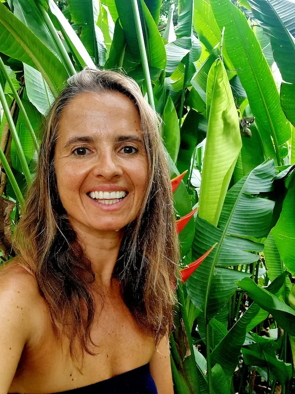 Close‑up portrait of a garden designer smiling in front of lush tropical leaves.