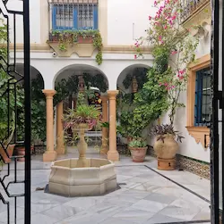 Patio tradicional con fuente central, vegetación y arquitectura mediterránea con azulejos y arcos