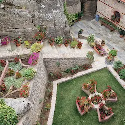 Patio ajardinado con césped, macetas y muros de piedra en entorno mediterráneo en monasterio en meteoras
